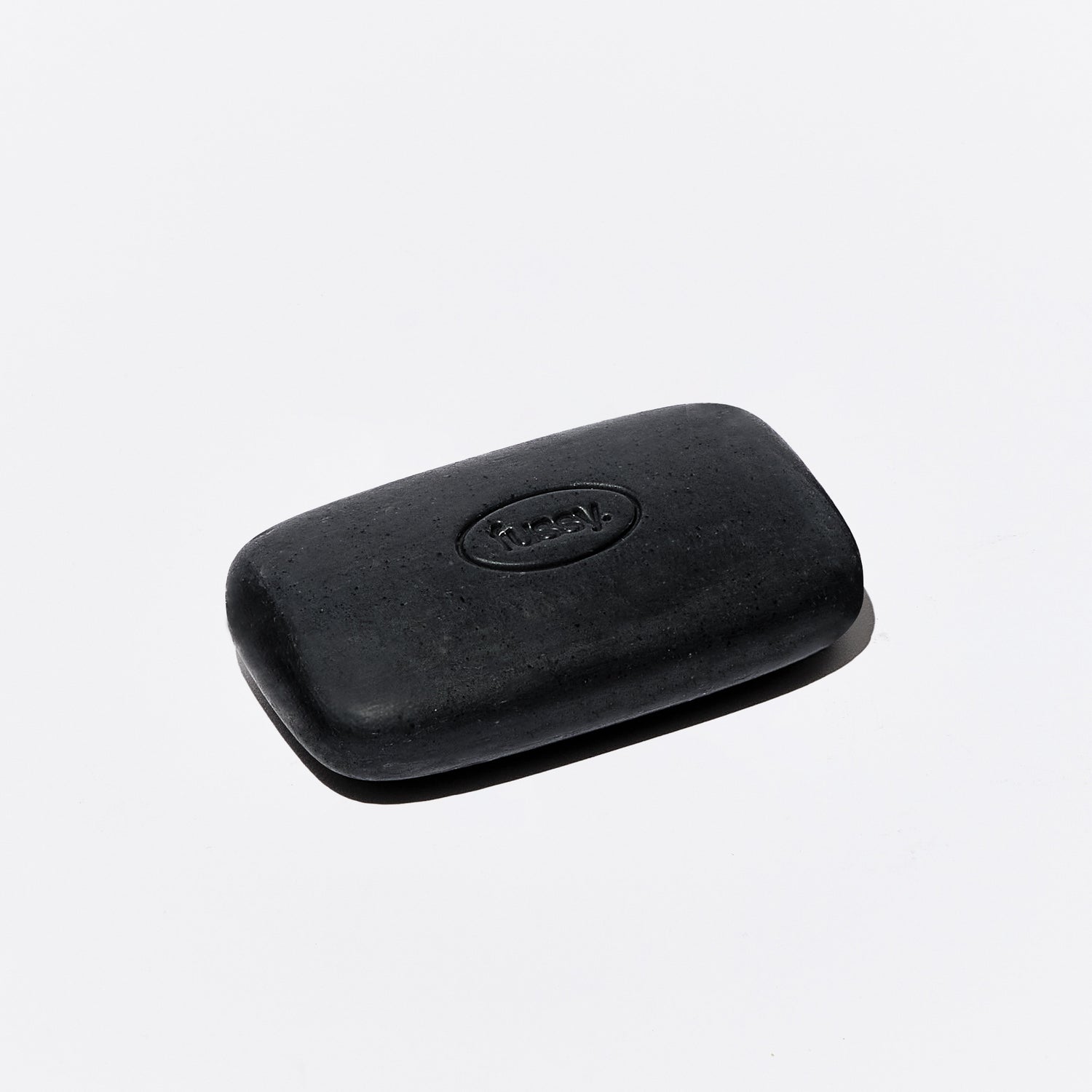 One singular, black exfoliating bar from Fussy, set at an angle.