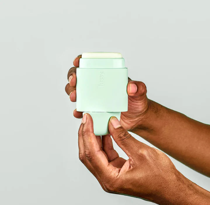 Two hands holding a Fussy deodorant  open case in Mint Green colour, demonstrating how to twist the bottom section to push up the deodorant for use.
